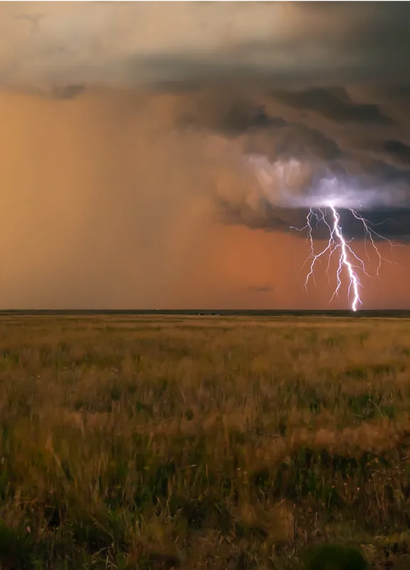 A lightning bolt illuminates the sky above a vast, open field during a stormy weather event.