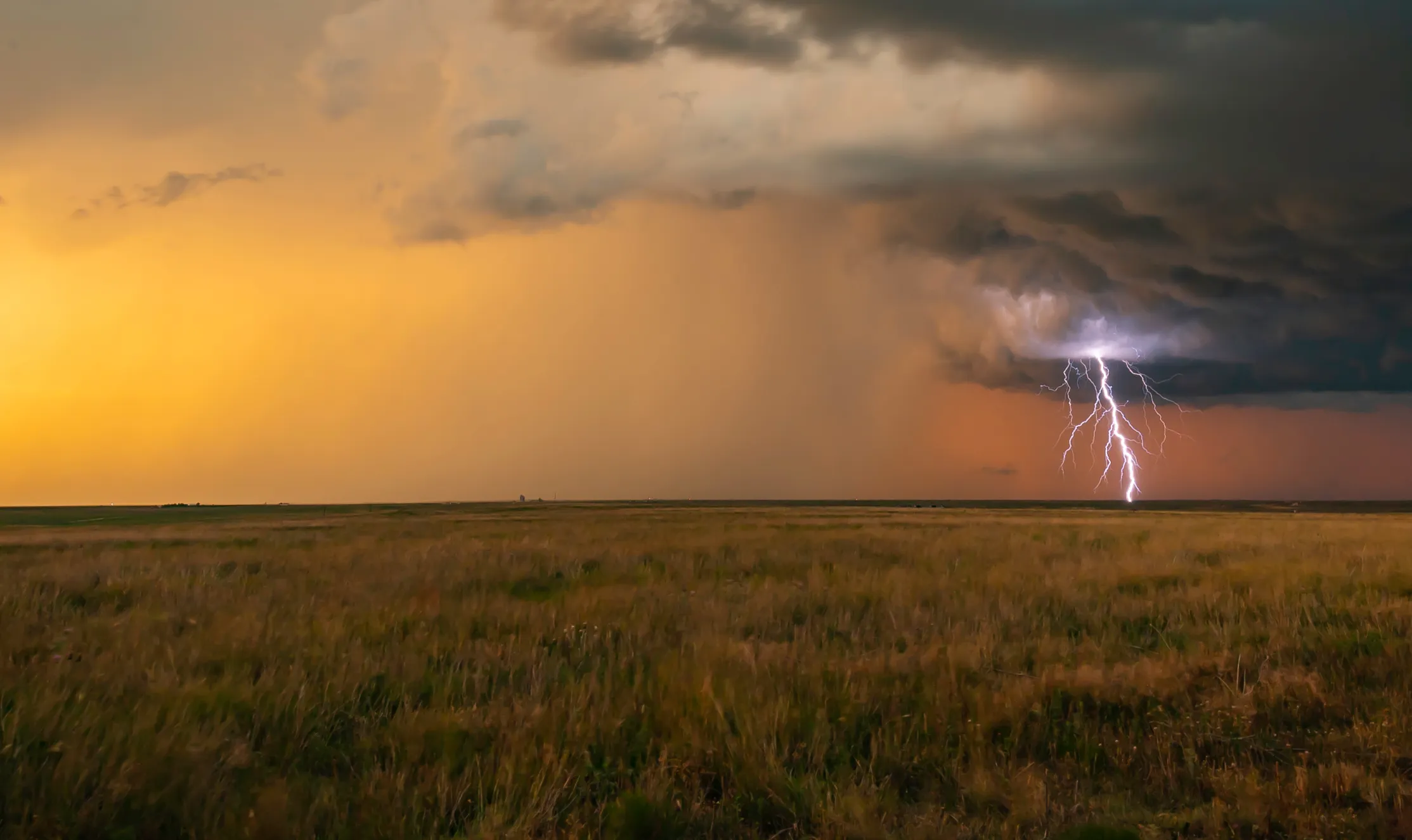 A lightning bolt illuminates the sky above a vast, open field during a stormy weather event.